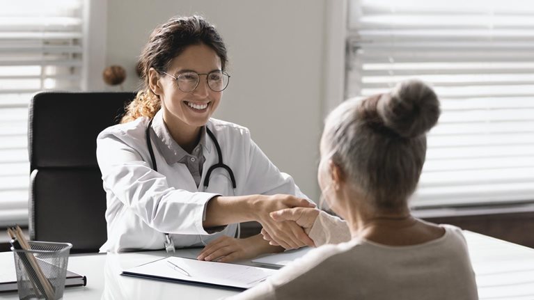 Young Hispanic female doctor shaking hand of senior woman patient