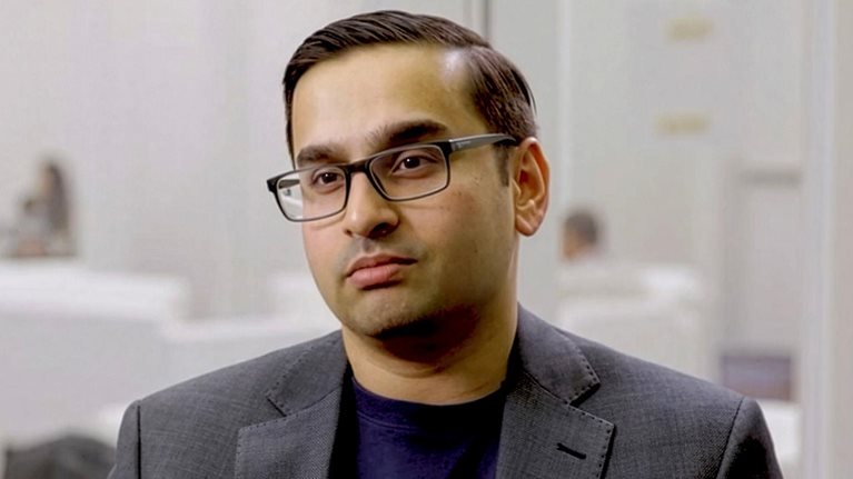 Ani Kelker wearing glasses and a dark blazer seated in a modern office during an interview.