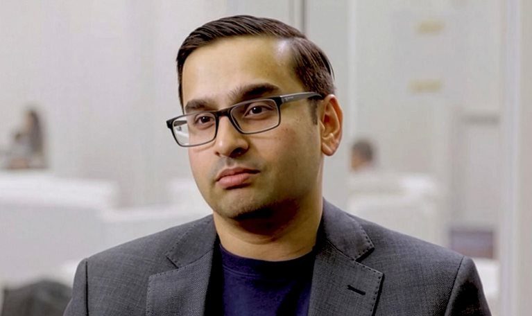 Ani Kelker wearing glasses and a dark blazer seated in a modern office during an interview.