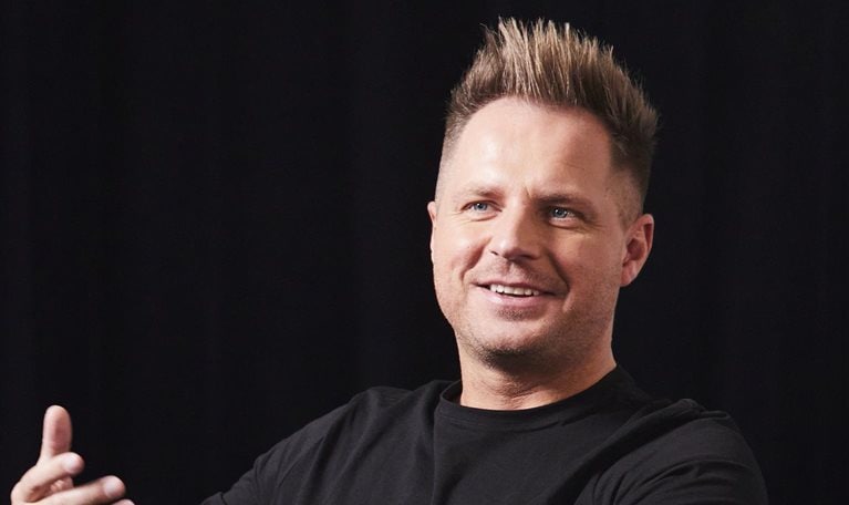 Photo of David Reger sitting on a couch on a stage, and gesturing with his hand while sharing an idea.