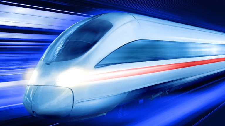 A sleek, modern high-speed train as it moves at great velocity through a dark, tunnel-like space. The motion is emphasized by the vibrant blue and white light trails that blur past the train.