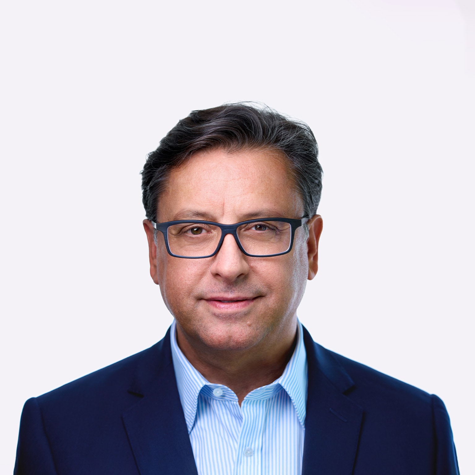 A man named Paul Hudson, sporting dark hair and glasses, can be seen in a slight smile as he faces the camera. He is dressed in a blue suit jacket and a striped blue shirt.