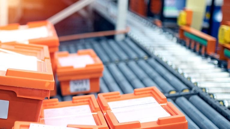Warehouse conveyor belt with orange crates that are being packed with medicine