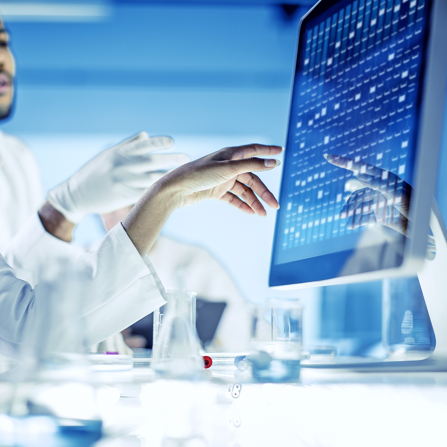 Close up image of scientists discussing and gesturing with their hands at data on a monitor.
