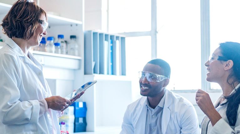 Chemist using tablet PC while talking to coworkers
