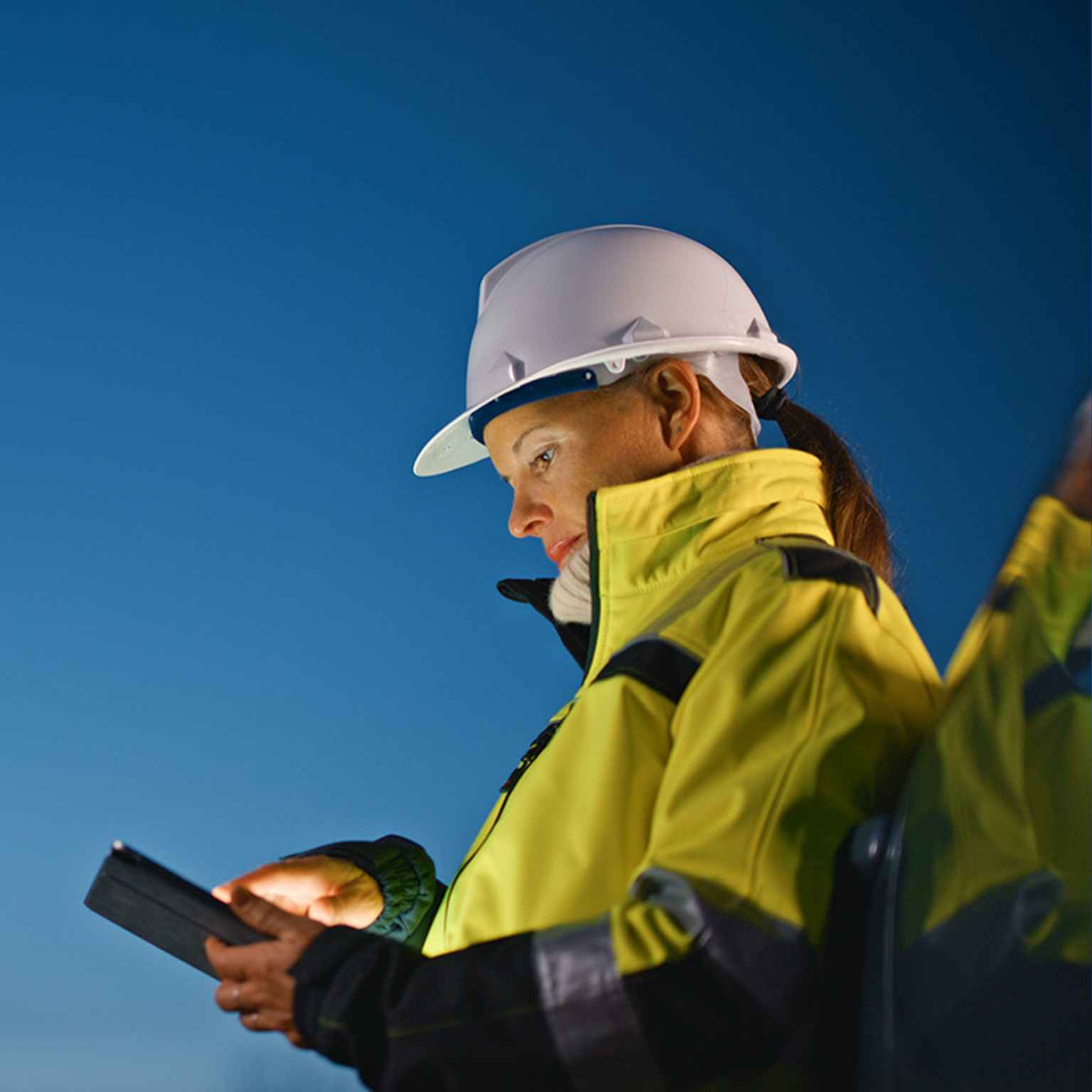 Female worker in protective workwear using tablet PC while standing by car at oil industry against sky