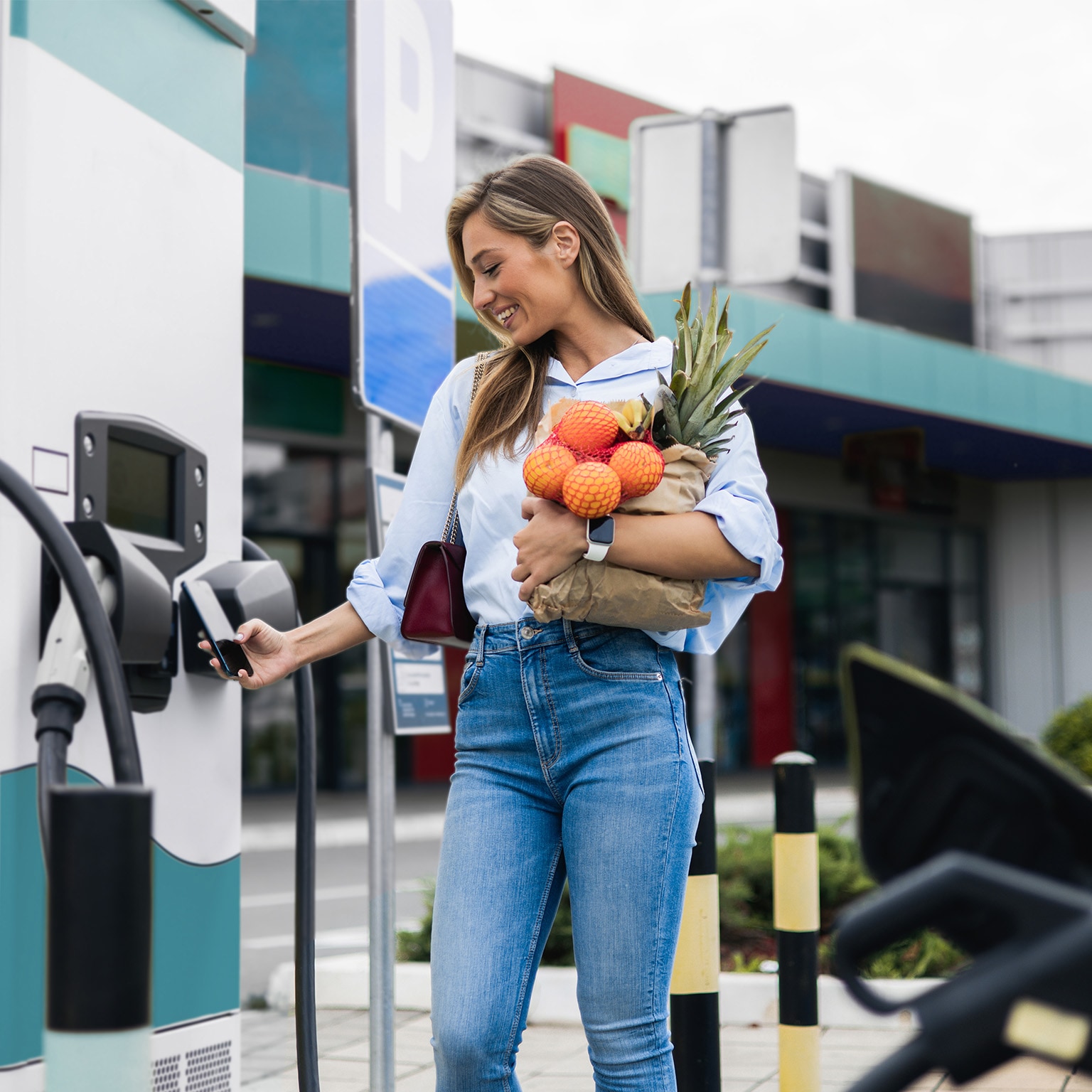 Happy young woman is charging an electric car in the parking lot - stock photo