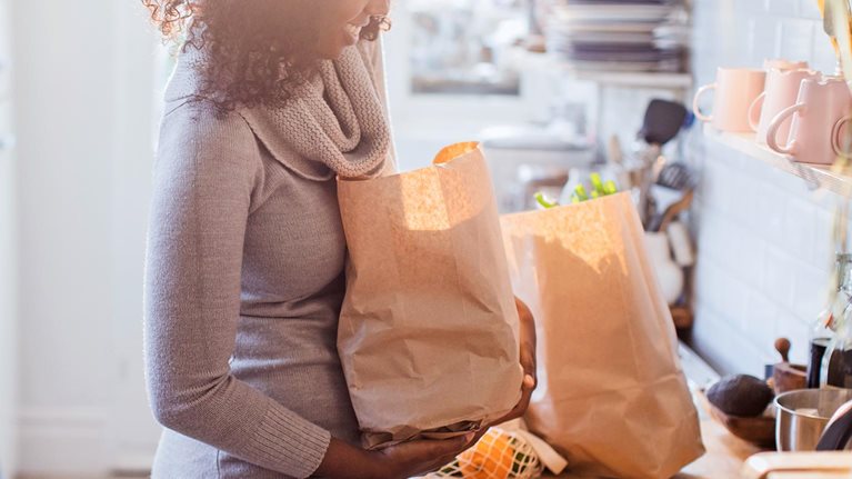 Mother and daughter unloading groceries in sunny kitchen - stock photo