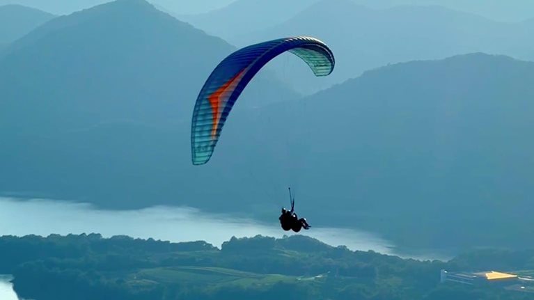 A person paraglides on high mountains overlooking the lake