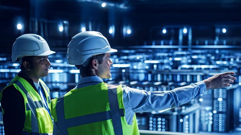 Two men in hard hats look out at a server farm in a data center