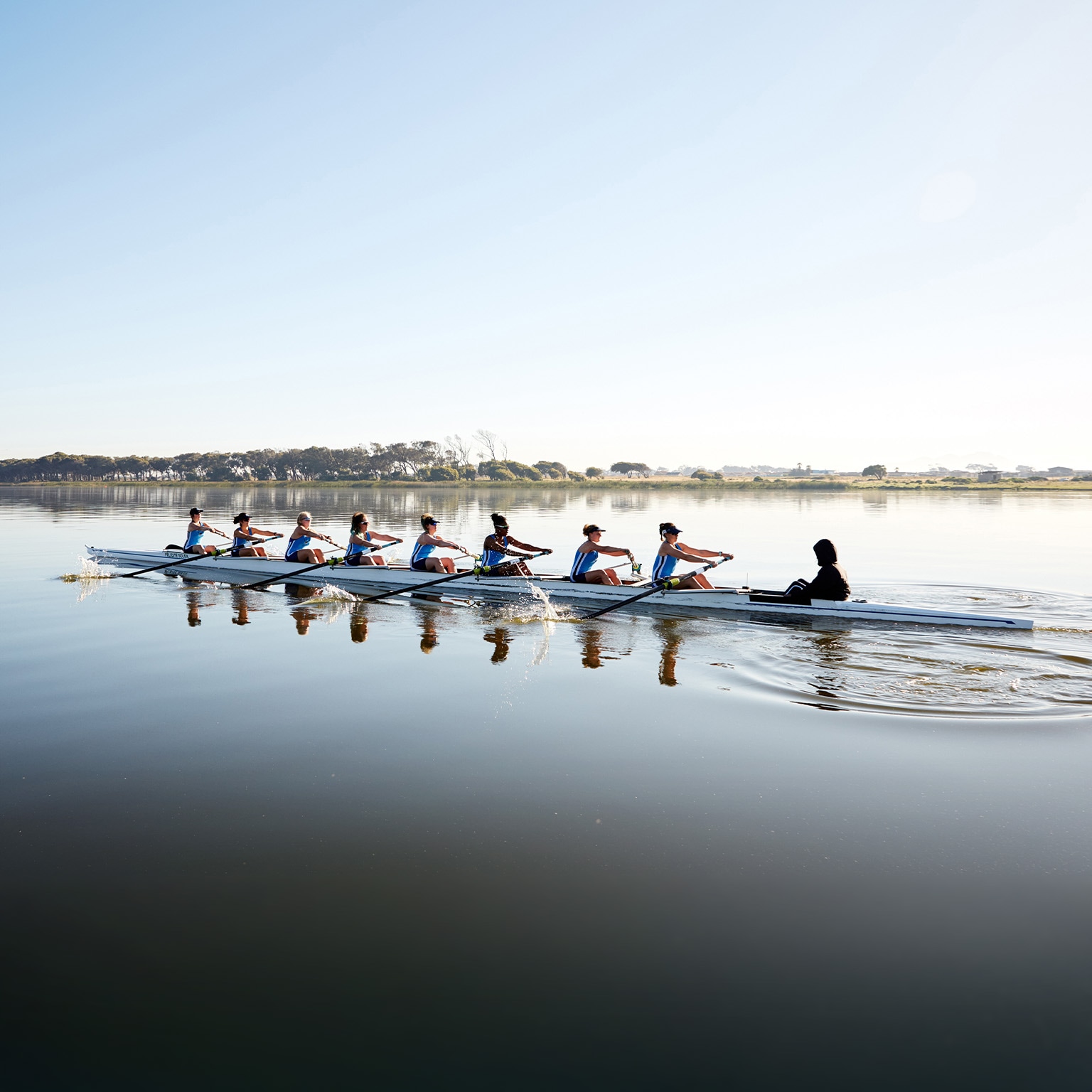 Female rowing team rowing scull on tranquil lake