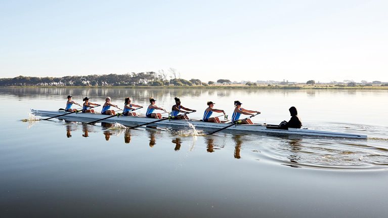 Female rowing team rowing scull on tranquil lake