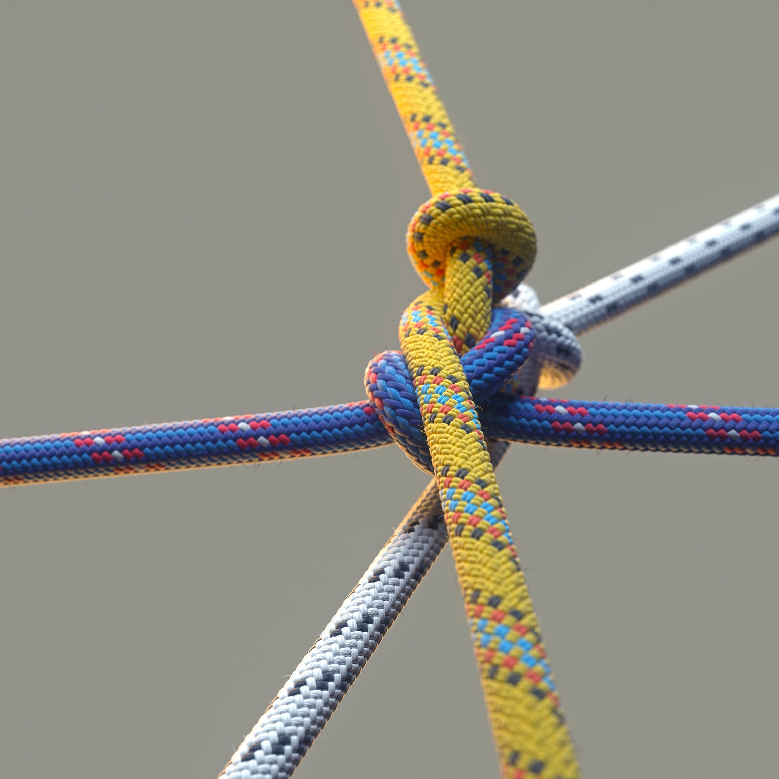 Close up image of three colored ropes knotting together on beige background.