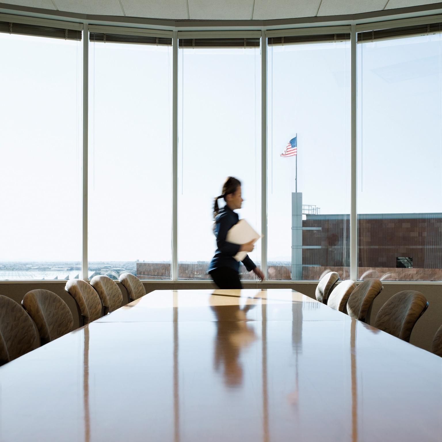 Hispanic businesswoman rushing through conference room, an American flag is seen though the window on top of an adjacent building