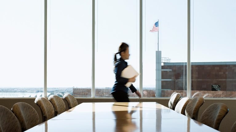 Hispanic businesswoman rushing through conference room, an American flag is seen though the window on top of an adjacent building