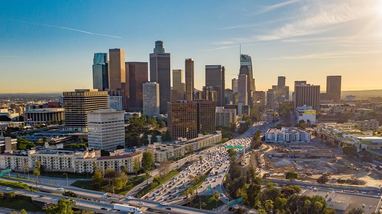 Drone view of downtown Los Angeles or LA skyline with skyscrapers and freeway traffic below.
