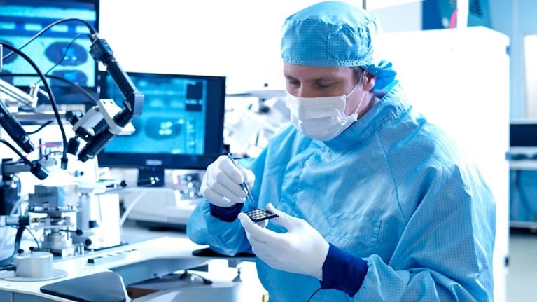 Electronics workers selecting chips at workstation in clean room laboratory