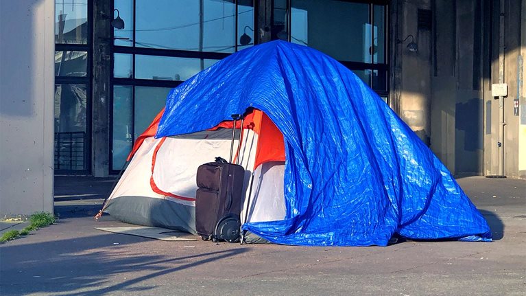 Tarped tent and suitcase on a city sidewalk