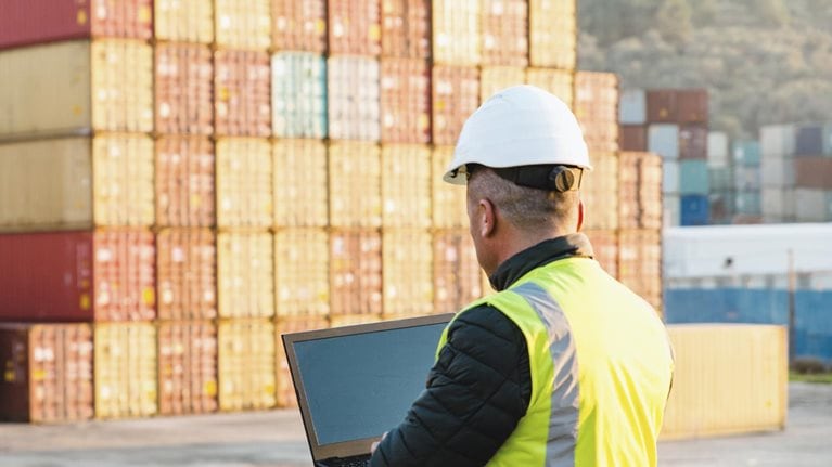 Engineer man with yellow crash helmet and worker west checking cargo freights in front of colorful cargo container stacks in shipping port