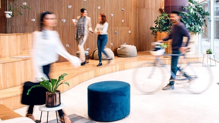 A building's reception, where people are engaged in many activities. A grayed out cycle and walkers are seen in the enclosure showing flexibility in the workplace.