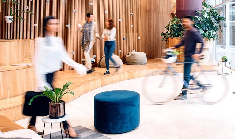 A building's reception, where people are engaged in many activities. A grayed out cycle and walkers are seen in the enclosure showing flexibility in the workplace.