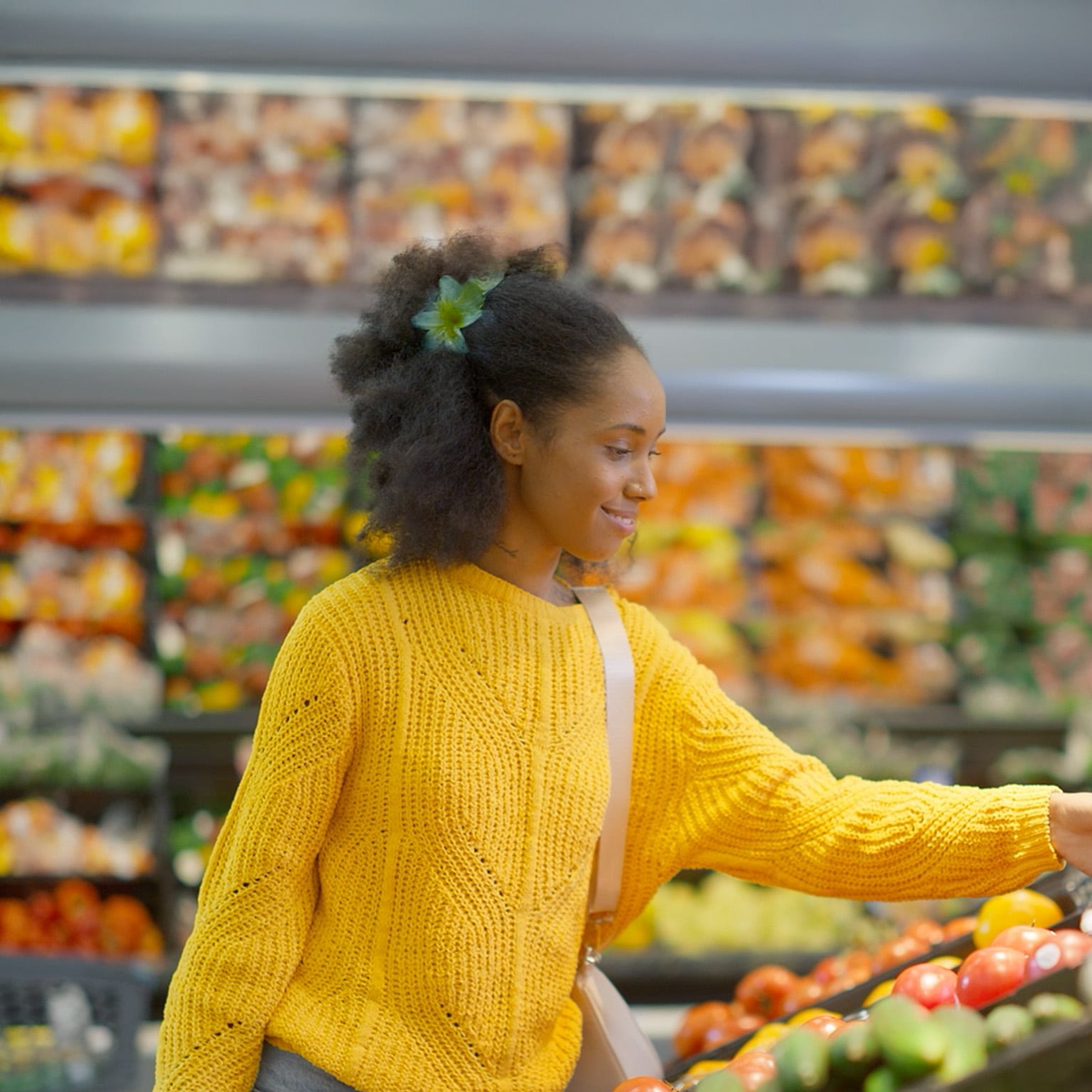 Woman in a yellow sweater shopping in the produce section of a supermarket 