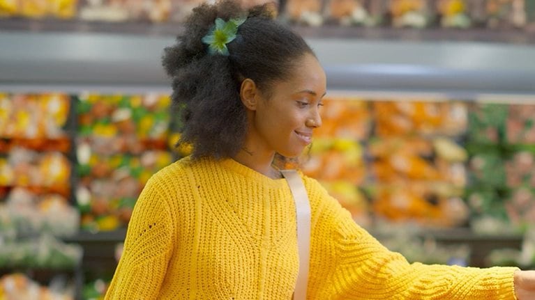 Woman in a yellow sweater shopping in the produce section of a supermarket