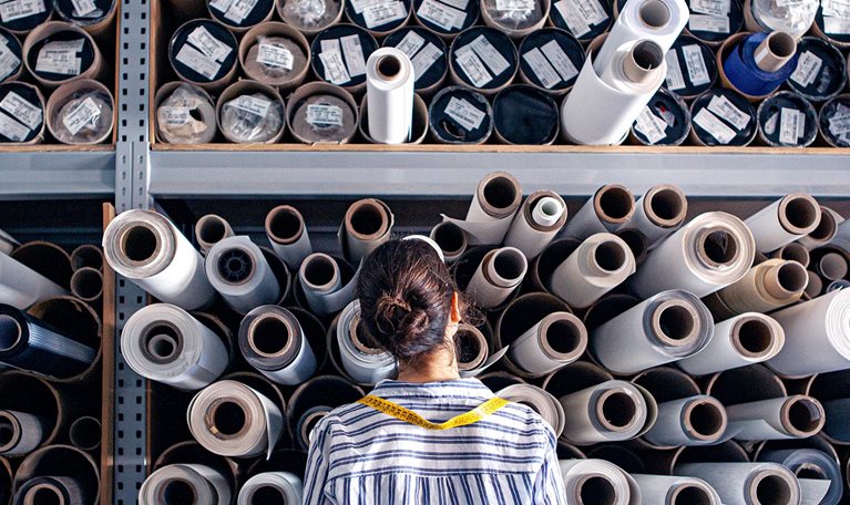 Portrait of textile designer choosing fabric from stack of rolls inside sustainable workshop.