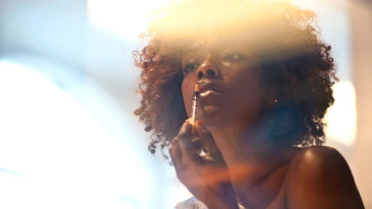 Black woman applying makeup in mirror