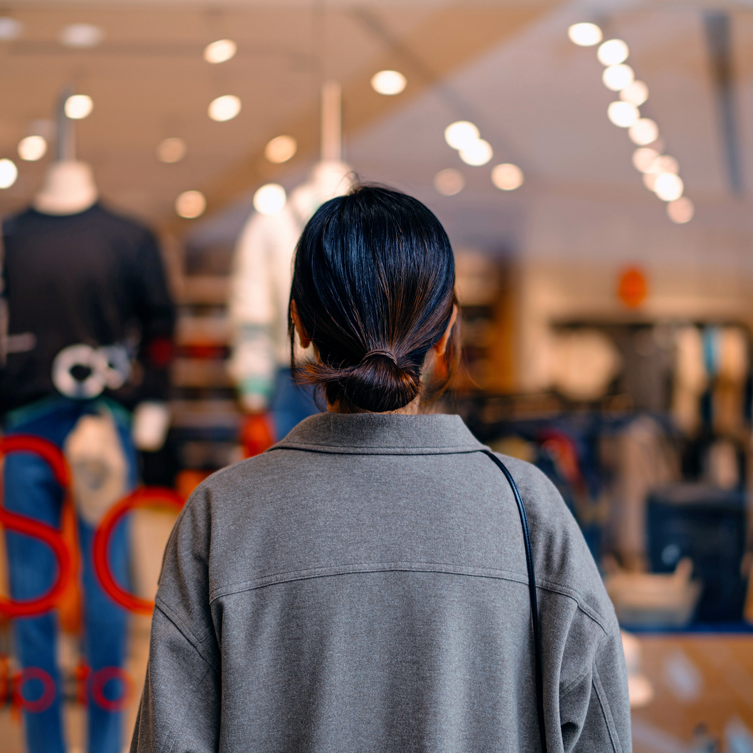 Rear view of young Asian woman standing outside a boutique looking at clothing through a shop window.