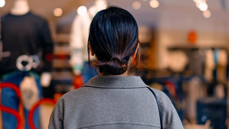 Rear view of young Asian woman standing outside a boutique looking at clothing through a shop window.