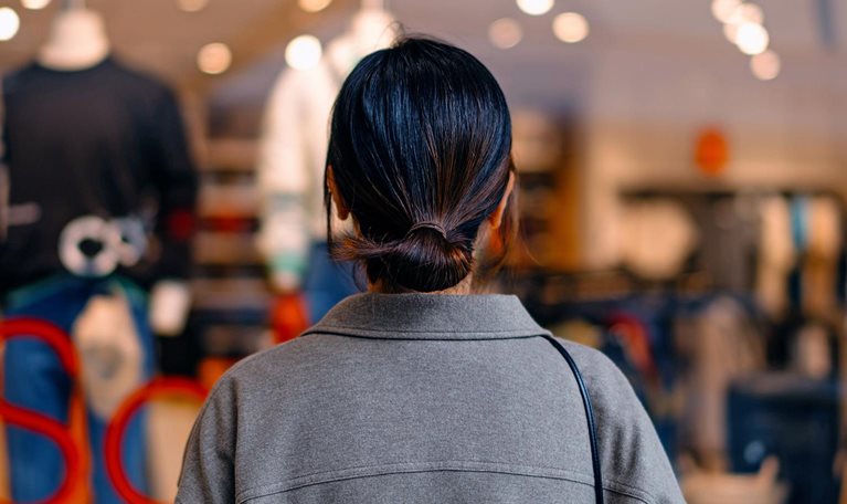 Rear view of young Asian woman standing outside a boutique looking at clothing through a shop window.