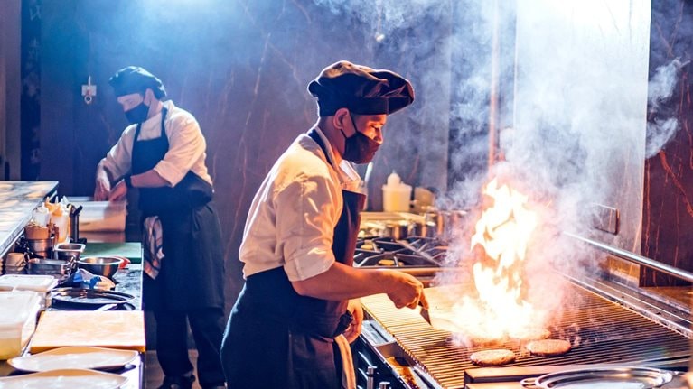 Chefs wearing protective face masks preparing a dish in restaurant kitchen