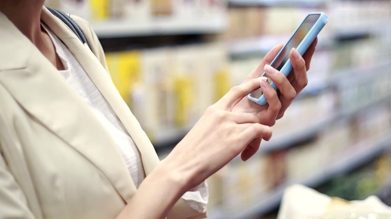 Woman using cell phone, grocery shopping in market - stock photo