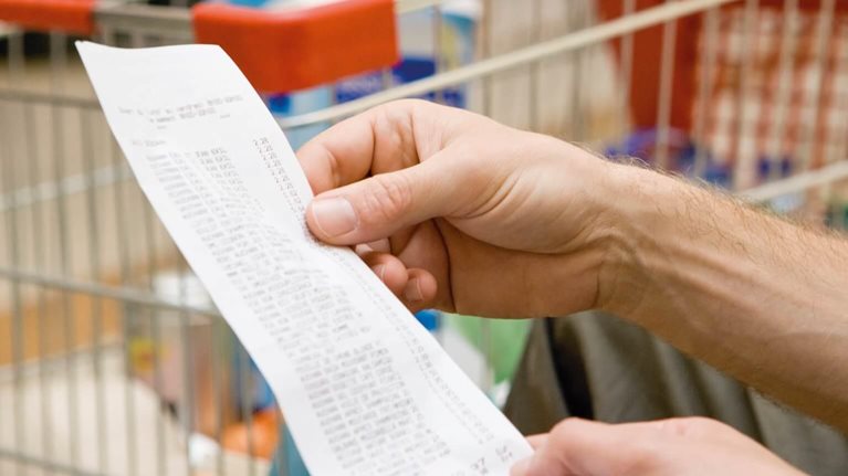 photo of hand holding grocery receipt in front of shopping cart