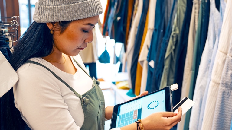 Retail shop clerk taking a mobile credit card payment on a digital tablet in a clothing boutique