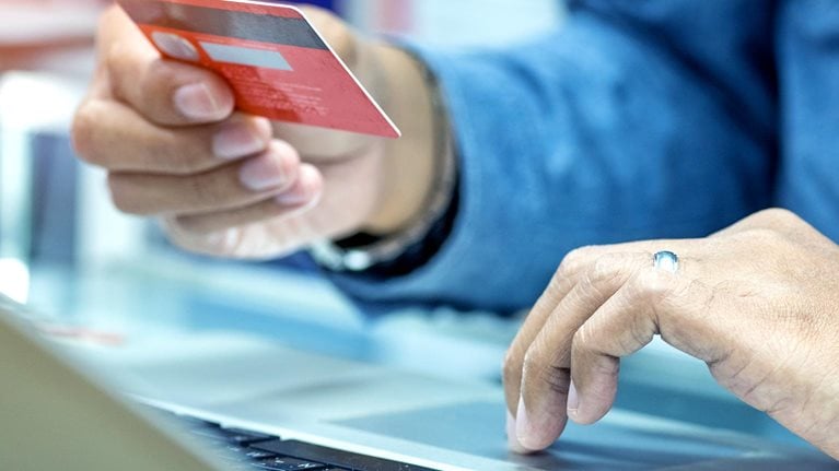 hand holding credit card in the air, other hand clicking laptop while online shopping - stock photo