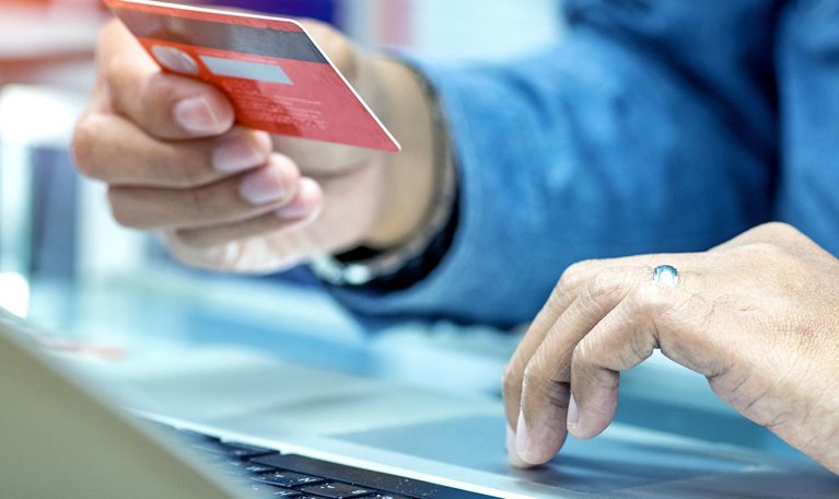 hand holding credit card in the air, other hand clicking laptop while online shopping - stock photo
