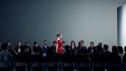 Female model walking on catwalk in front of crowd at fashion show.
