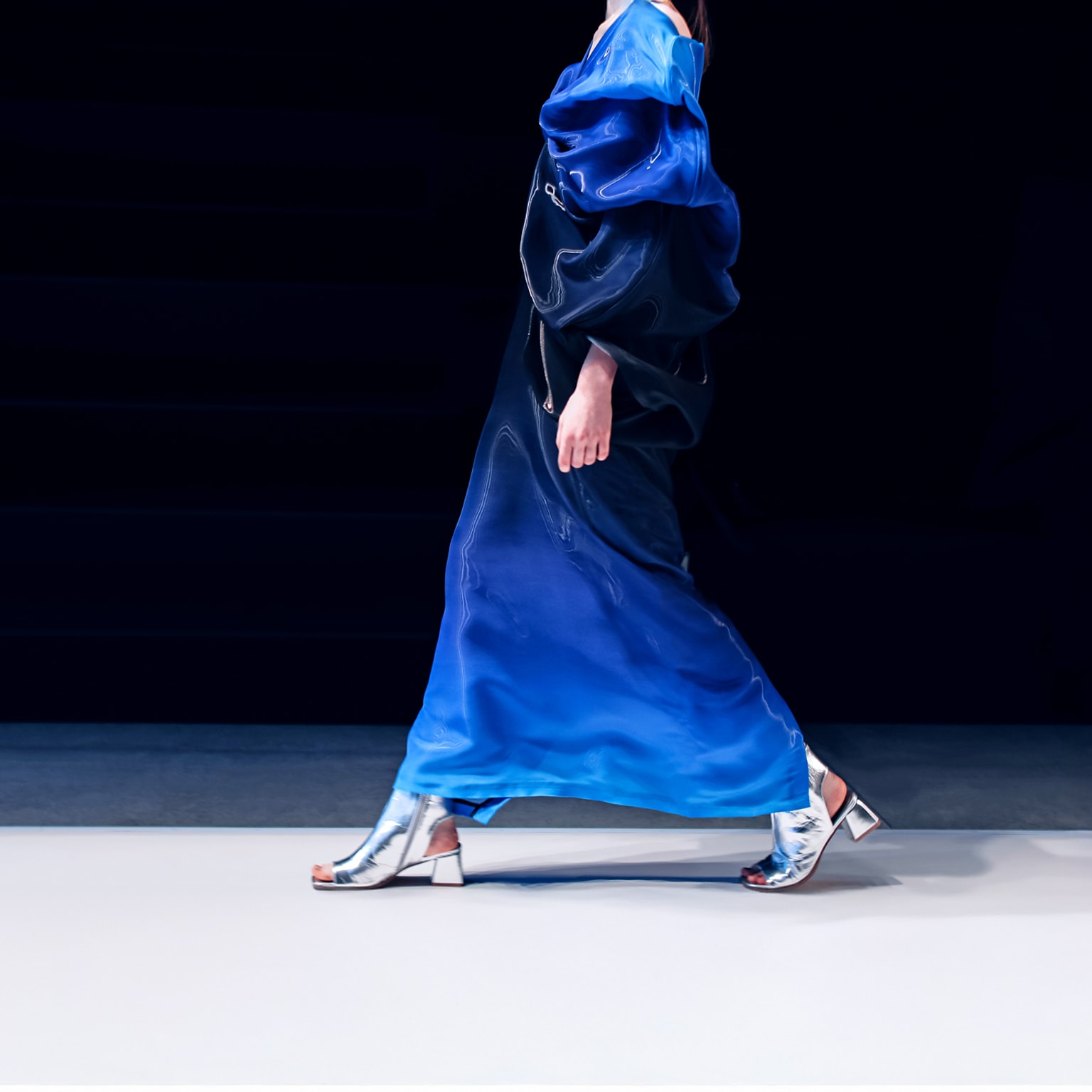 A woman struts down the runway in a creative blue designer satin dress