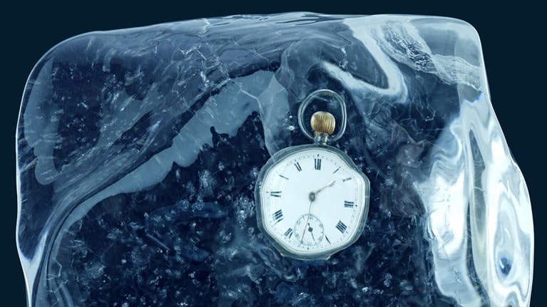 A pocket watch encased in a block of ice and set against a deep blue backdrop.