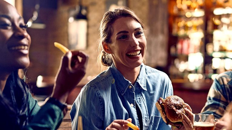 Multiracial group of happy friends eating burgers while drinking beer in a pub.