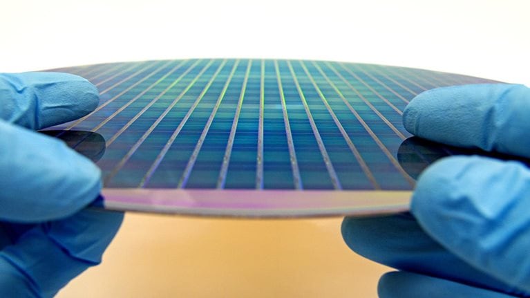 Image of gloved hands holding a patterned 300 mm silicon wafer.