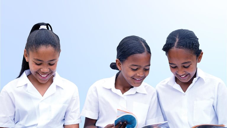 Schoolgirls looking through textbooks in school yard together