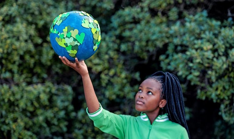 Young African girl holding up a homemade globe of green heart shapes