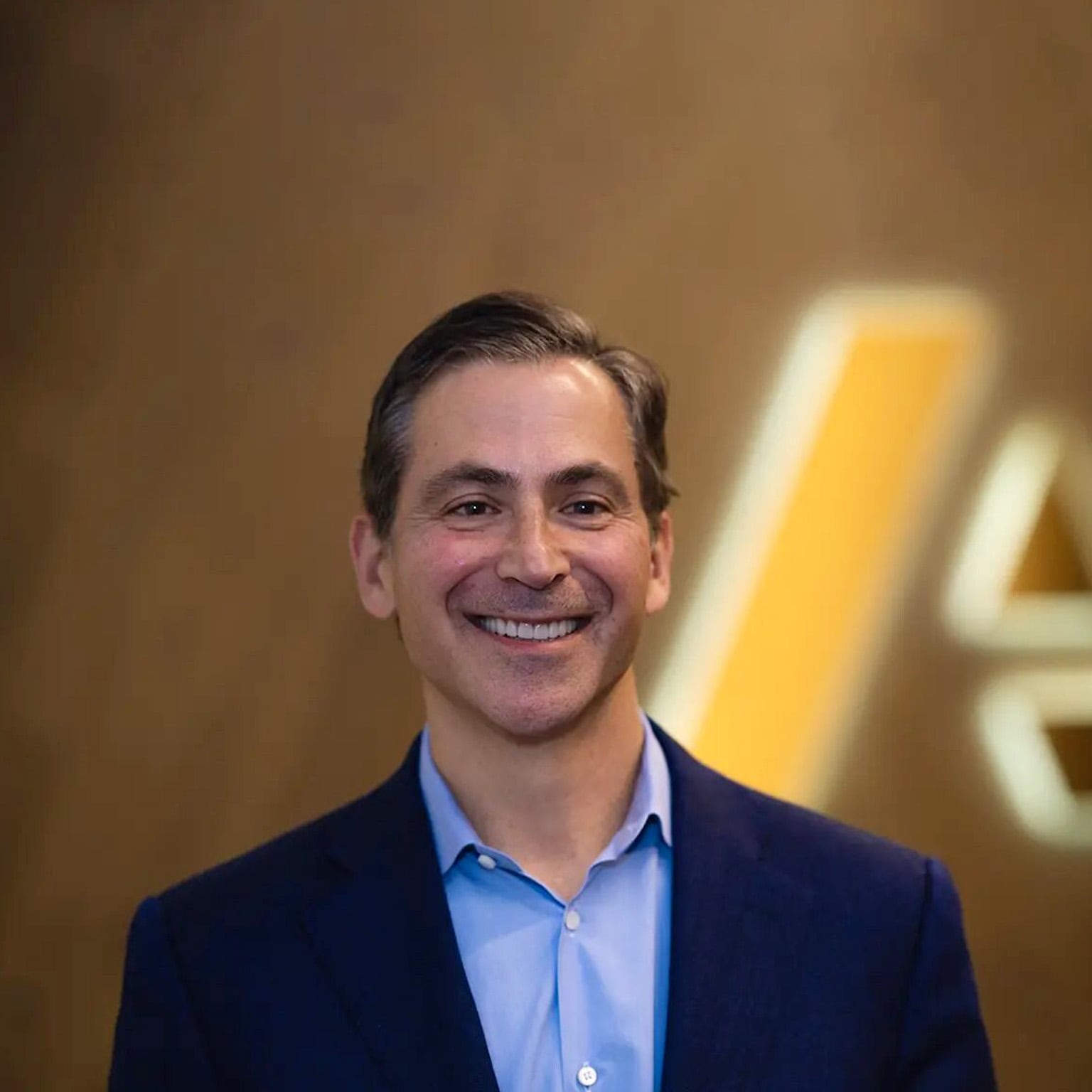A smiling Charlie Gottdiener dressed in a suit coat and button-up shirt, set against a blurred backdrop featuring the Anaplan logo.