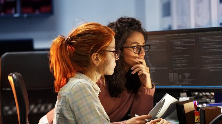 Two female programmers working on new project. They working late at night at the office. - stock photo
