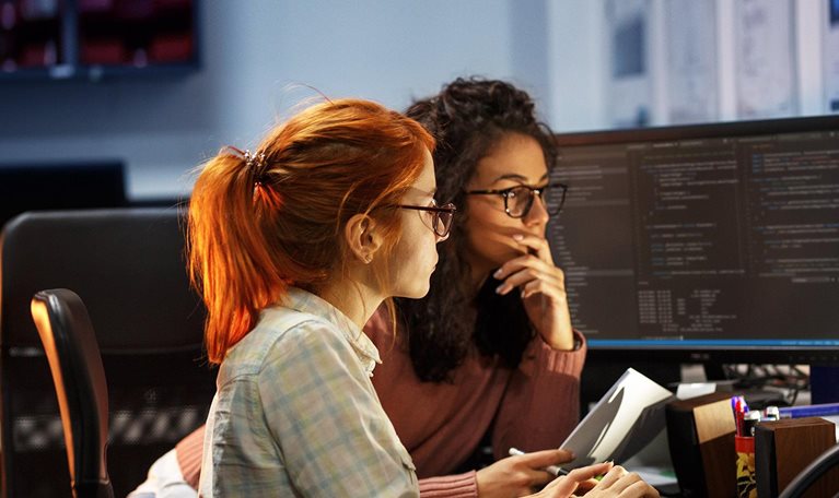 Two female programmers working on new project. They working late at night at the office. - stock photo