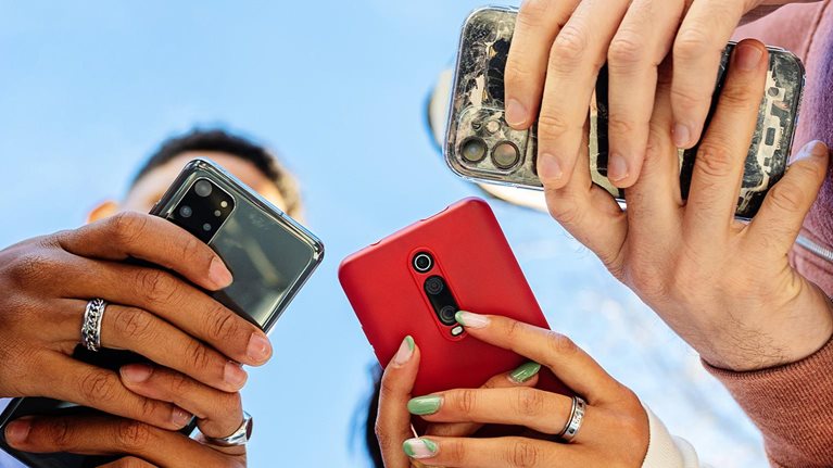 Low angle view of three young people using mobile phones outdoors - stock photo
