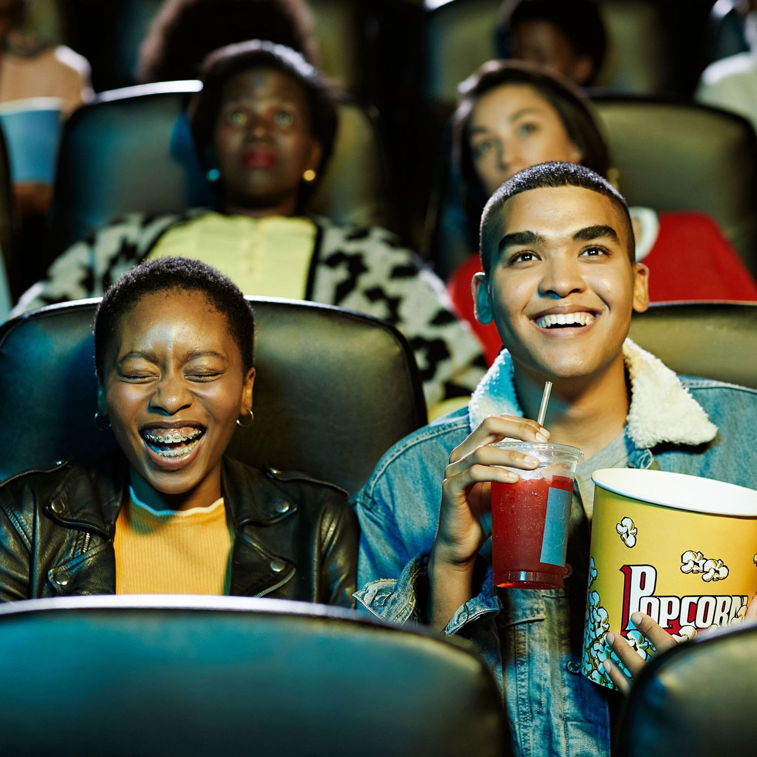 Cheerful young friends watching movie in theater.